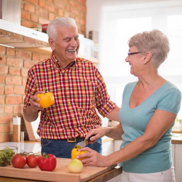 An older couple cook together while smiling.