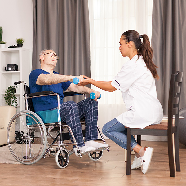 An older man in a wheel chair is doing physical therapy with a caregiver.